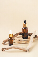 Two brown bottles of cosmetics on a natural beige background. A stone podium and a driftwood. Front view.