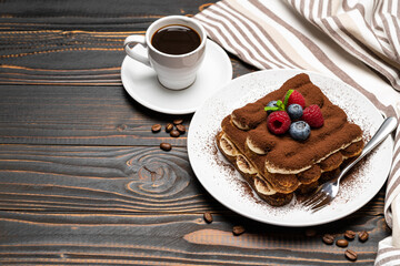 portion of Classic tiramisu dessert with raspberries, blueberries and cup of espresso coffee isolated on wooden background