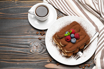 portion of Classic tiramisu dessert with raspberries, blueberries and cup of espresso coffee isolated on wooden background
