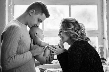 Young women and a man hold a naked newborn in their arms near the window.
