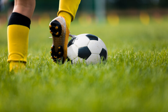 Closeup of soccer player running and kicking soccer ball on grass lawn. Legs of footballer playing competition match. Sports horiznotal background. Athlete in soccer cleats and soccer socks