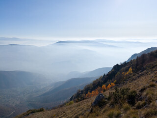 Scenic view from Vlašić mountain to the valley filled with fog and mountain peaks above the fog in autumn during a sunny day