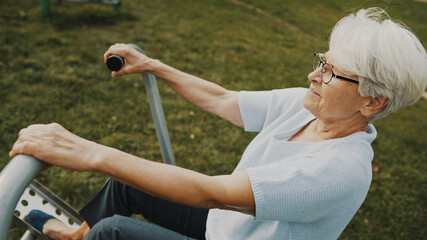 Old woman exercising in and outdoor gym. . High quality photo