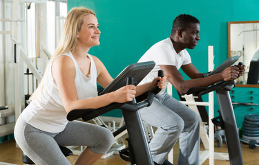 African man and Caucasian woman exercising on stationary bikes at gym