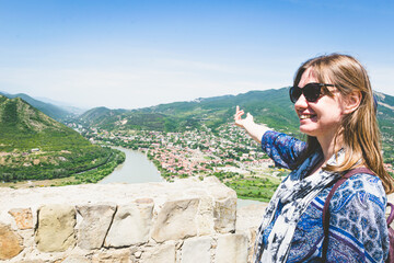 Young female woman in blue dress points finger to Mtskheta town in Georgia.Torusim and travel in...