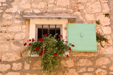 Fototapeta na wymiar old stony wall with window decorated with flowers , rovinj, croatia