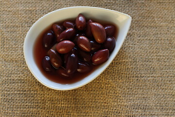 Olives kalamata on white plate with dark marinade. Special Greece receipt of olives. 
