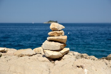 Fototapeta na wymiar stone tower made of rocks in balance at the beach with blue sea in the background, Rovinj, Croatia