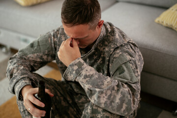 Fototapeta premium Depressed soldier with bottle sitting in livig room., Alcohol addiction...