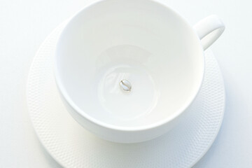 pendant made of silver in the form of a coffee bean, at the bottom of a white porcelain mug, on a white background. Jewelry, pendant for coffee lovers. Memorable gift, relationship, love. Coffee day.