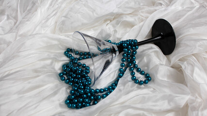 Turquoise faux pearl necklace on white silk background with martini glass.