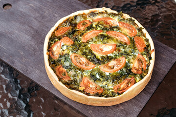 Pie with spinach and tomatoes lies on table. Homemade pie for the whole company made from vegetables.