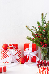 Gift boxes and red balls , fir tree branches and hawthorn twigs in a vase on white wall background, new year and christmas concept