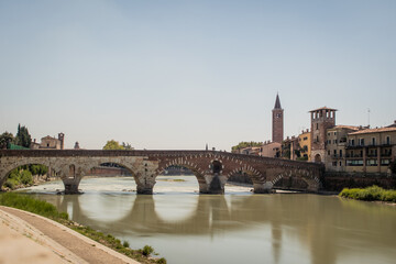Fototapeta na wymiar view of the famous Ponte Pietra in Verona, rising above the river of Adige in Italy. Long exposure daylight shot on a sunny day of an old brick bridge.