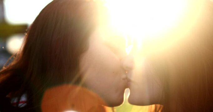 Girlfriends kissing outside in the sunlight lens-flare. Two young women kiss