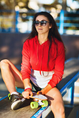 Young woman in sunglasses is resting on the sports ground for skateboarding on a summer sunny evening