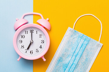 Pink alarm clock and medical mask on a colored background. Concept on the topic of quarantine