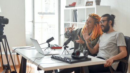 Female and male blogger saying hello, greeting subscribers while recording video blog or vlog at home. Man and woman making music using synthesizer, drum pad machine