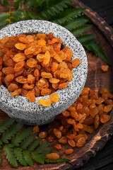 Close up of yellow raisins in a stone bowl, close up, dark background