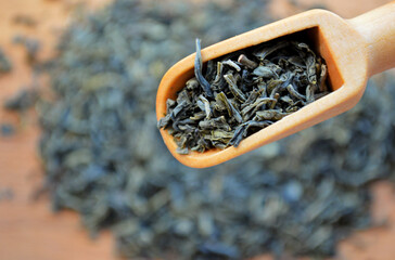 Wooden spoon with loose leaf tea on blurred heap of tea background.