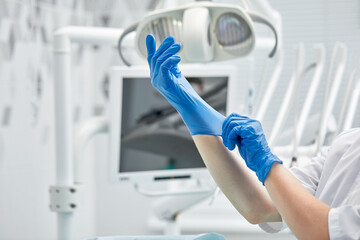 A female dentist puts on gloves against a background of dental equipment in a dental office. Happy patient and dentist concept.