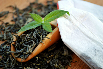 Tea bags and a wooden spoon with fresh mint leaves lie on a heap of tea on a wooden background