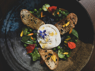 A gourmet Mozzarella plate with brown bread, peas, herbs and audible flowers.