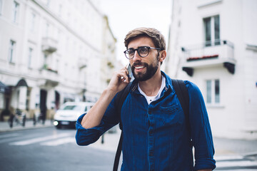 Cheerful man crossing road and talking on cellphone on street