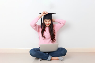 Young attractive Asian woman sitting with laptop on her legs wearing graduated hat, online education class, scholarship study abroad concept.