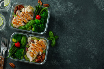 Healthy meal prep containers with green beans, chicken breast and broccoli. A set of food for keto diet in lunchbox on a dark concrete background. Top view with copy space