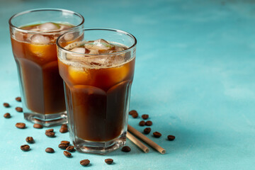 Ice coffee in a tall glass with cream poured over and coffee beans on a light stone background. Cold summer drink with tubes. With copy space