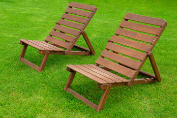 Recreation and tourism advertising. Two Empty brown wooden deck chair or chaise longue, on the green grass of a fresh lawn. Place for text