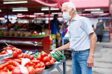 retired european man wearing medical mask protecting against virus buying tomatoes in market