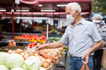 mature european man wearing medical mask protecting against the virus buying potatoes in market