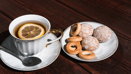 Snacks and sweets for tea in a small white saucer. Beautiful tea set. White ceramic Cup of tea with lemon on a wooden table.