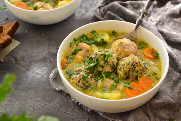 Meatball soup with noodles and carrots. Dark gray background. Gray linen napkin. Close-up. Healthy lunch, soup with herbs and meat.