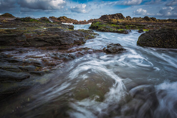Sea wave flowing view on volcanic rock beach in long exposure shot