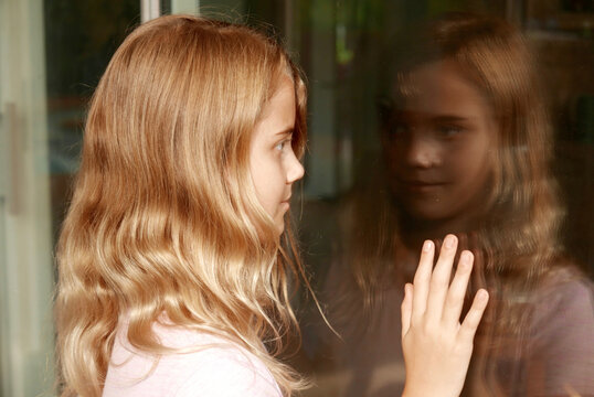 Girl smiling as she looks at her reflection in a sliding glass door