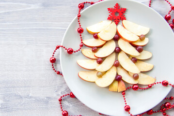 Christmas tree made of cut apples and berries with a large red, wooden snowflake instead of a star. A plate of apples is decorated with red beads.