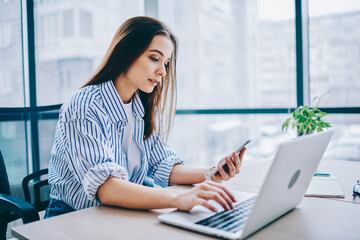 Millennial female trainee checking time on modern smartphone gadget during trial work day in modern...