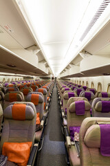 Looking down the aisle of a wide modern wide body jet aircraft, overhead bins open and empty economy seats waiting for passengers.