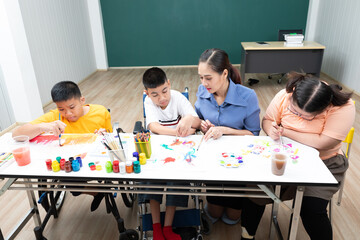 asian group of disabled kids or autism child learning and painting at paper with teacher helping in...