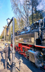 Steam locomotive with a driver at a water station.