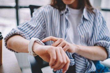 Cropped picture of woman checking received notification for update on digital wearable wrist watch, selective focus on female hands and new modern smartwatch looking for time to end of work