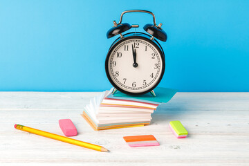 Alarm clock and school supplies on wooden desk