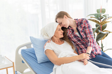 The senior breast cancer patient wearing a headscarf laying in bed  and her daughter touching each...