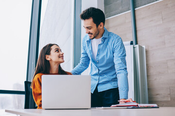 Happy Caucasian man and woman in smart casual apparel discussing graphic design for website enjoying positive collaboration in office, successful employees brainstorming on netbook application