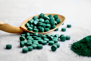 Pills of seaweed spirulina, chlorella on a wooden spoon close up. Vegetarian Super food with plant protein on light background