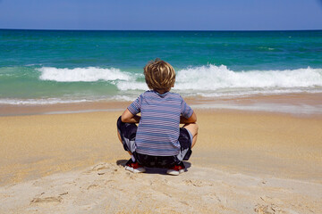 Boy crouching on a Florida beach, looking out at the turquoise ocean
