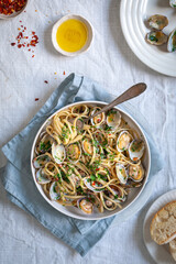 Top down view of pasta vongole, linguini with clams red pepper flakes and olive oil on white background with blue napkin